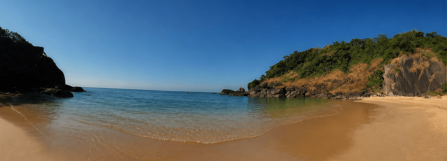 A sandy Goa beach with clear blue water and rocky, green headlands